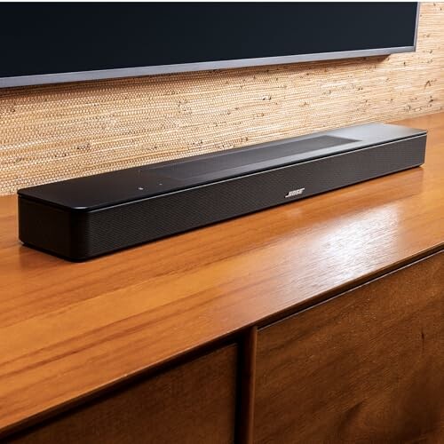 Black soundbar placed on a wooden surface below a TV.