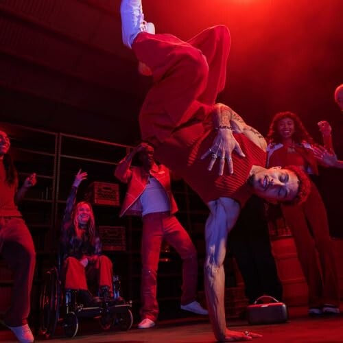 Breakdancer performs under red lighting with a cheering group.