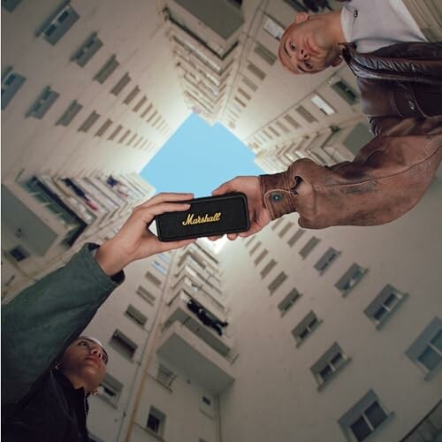 Two people holding a Marshall speaker in a building courtyard