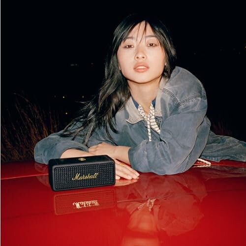 Person leaning on a red surface with a Marshall portable speaker