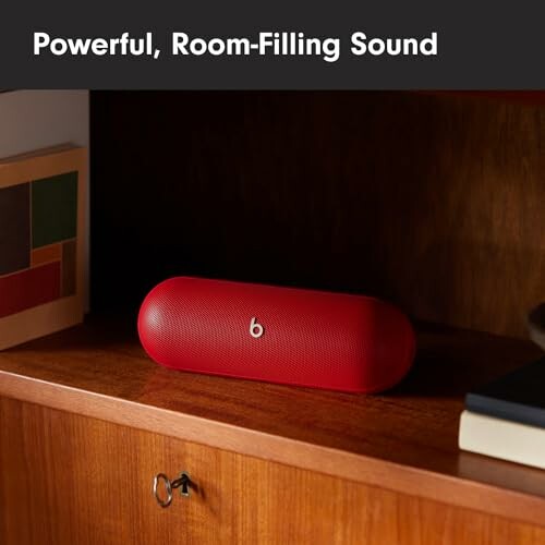 Red portable speaker on wooden shelf with books