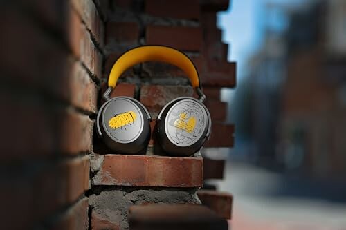 Yellow headphones resting on a brick wall outdoors.